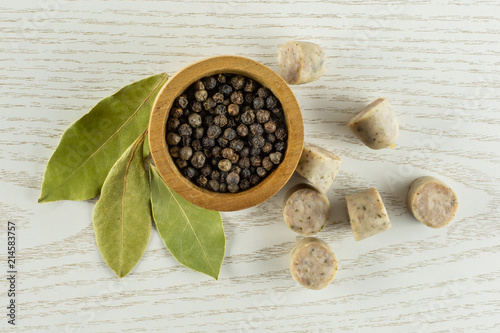 Lot of slices lot of pieces of bavarian white sausage with black pepper in a wooden bowl and three bay laurel leaves flatlay on grey wood photo