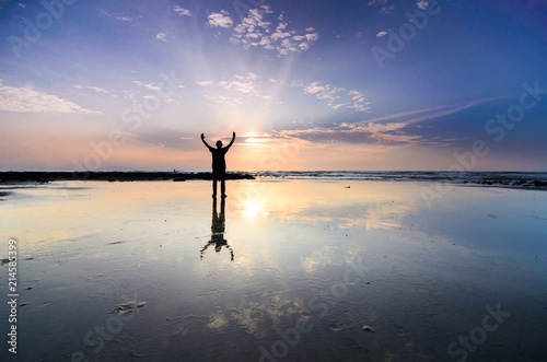 Silhoutte of man raise hand above facing the sunrise with water reflection