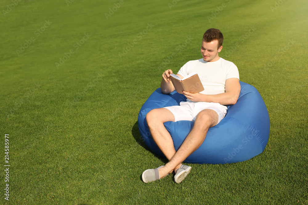 Young man reading book while sitting on bean bag chair outdoors Young man reading book while sitting on bean bag chair outdoors