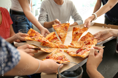 Young people taking slices of hot tasty pizza from cardboard box © Pixel-Shot