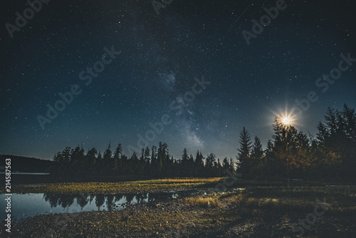 Milky Way galaxy night sky over forest with moon and reflection. Vancouver Island, Tofino, Canada