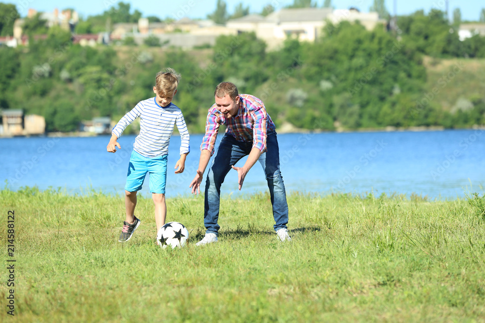 Happy father and son playing football near river Happy father and son playing football near river