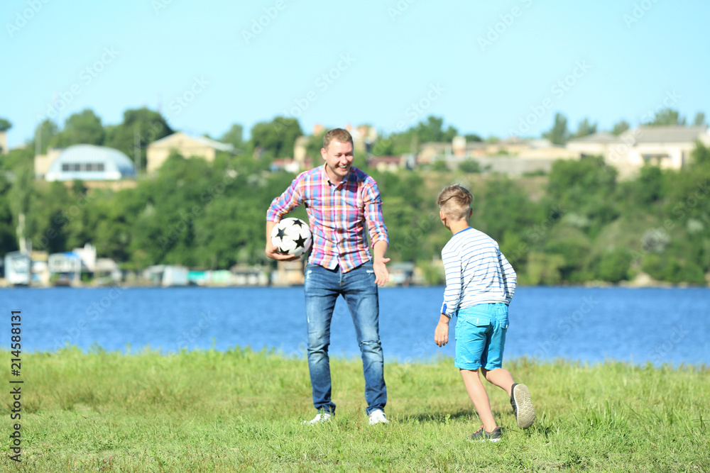 Happy father and son playing football near river Happy father and son playing football near river