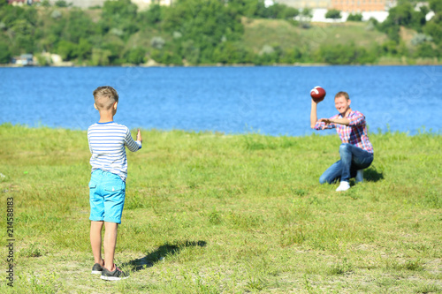 Happy father and son playing rugby near river © Pixel-Shot