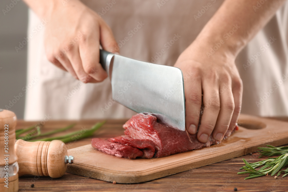 Man cutting raw meat on wooden board in kitchen