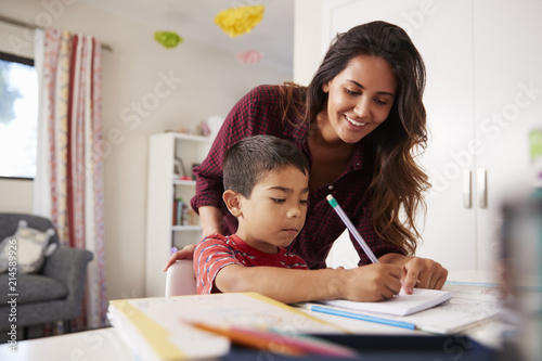 Mother Helping Son With Homework Sitting At Desk In Bedroom photo