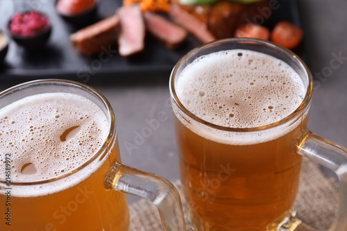 Mugs with fresh tasty beer on table, closeup