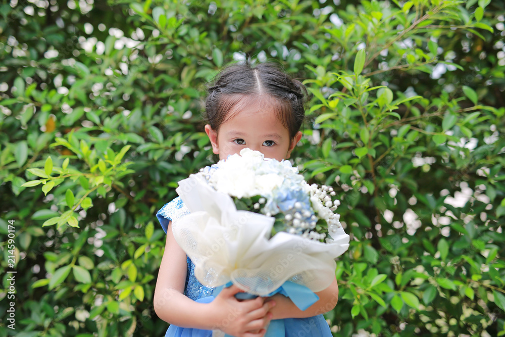 Portrait of cute little child girl smelling Bouquet of flowers in the garden.