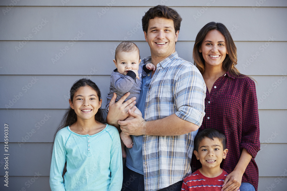 Obraz premium Portrait Of Happy Family With Baby Standing Outside Grey Clapboard House
