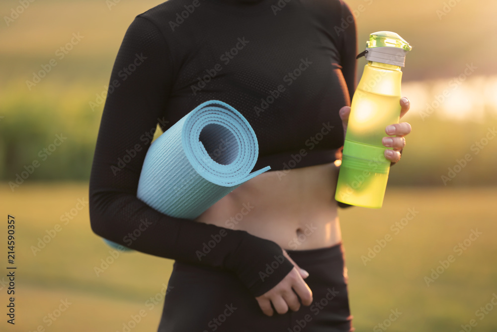 Beautiful young woman with bottle of water and yoga mat outdoors in the morning Beautiful young woman with bottle of water and yoga mat outdoors in the morning