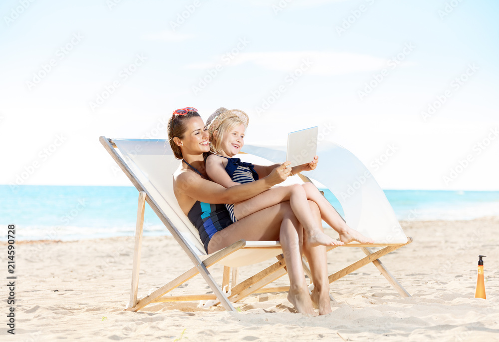mother and daughter using tablet PC while sitting on beach chairs