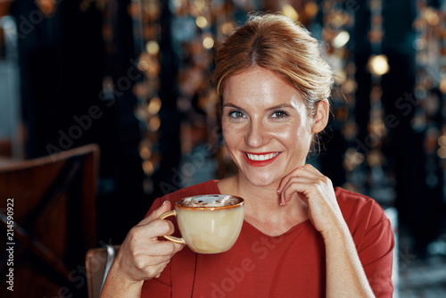 Portrait of beautiful smiling woman holding a cup of cappuccino and enjoying the moment