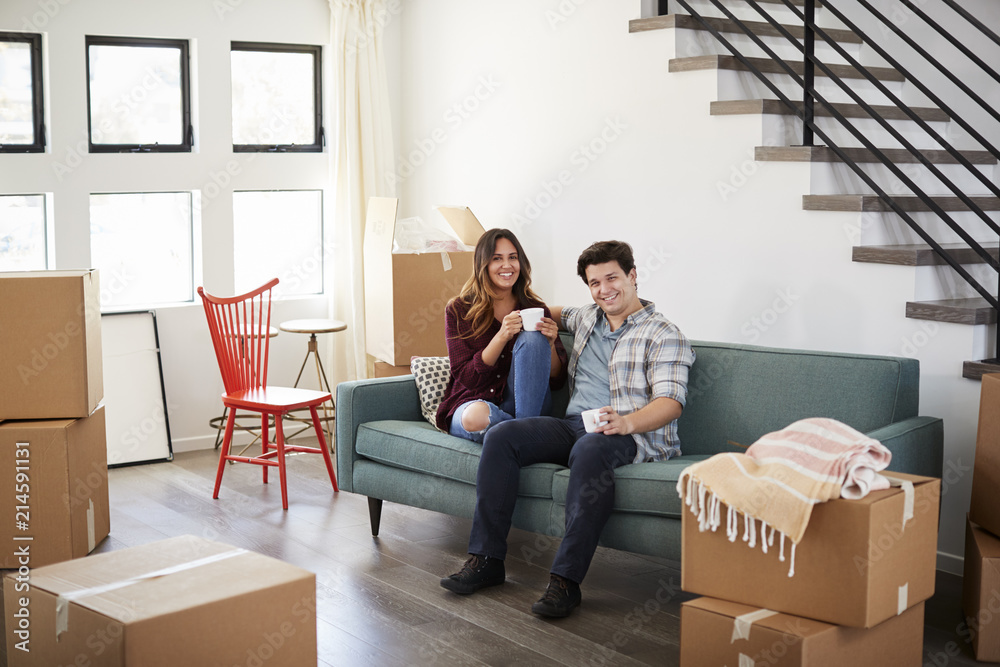 Portrait Of Happy Couple Resting On Sofa Surrounded By Boxes In New Home On Moving Day Portrait Of Happy Couple Resting On Sofa Surrounded By Boxes In New Home On Moving Day