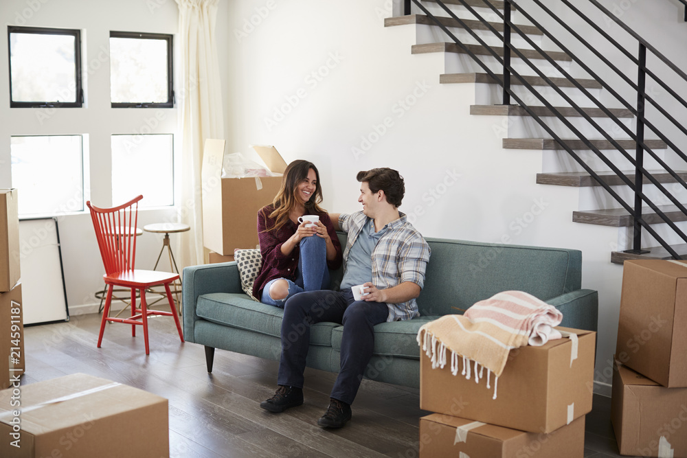 Happy Couple Resting On Sofa Surrounded By Boxes In New Home On Moving Day Happy Couple Resting On Sofa Surrounded By Boxes In New Home On Moving Day