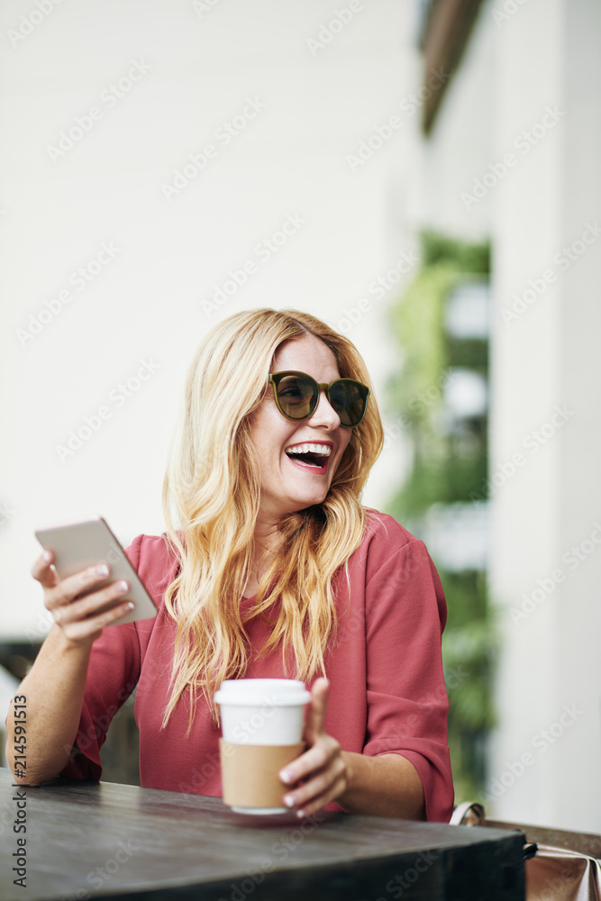 Happy woman wearing sunglasses while resting at street cafe with mobile phone and drinking coffee Happy woman wearing sunglasses while resting at street cafe with mobile phone and drinking coffee
