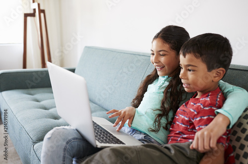 Brother And Sister Sitting On Sofa At Home Having Fun Playing On Laptop Together