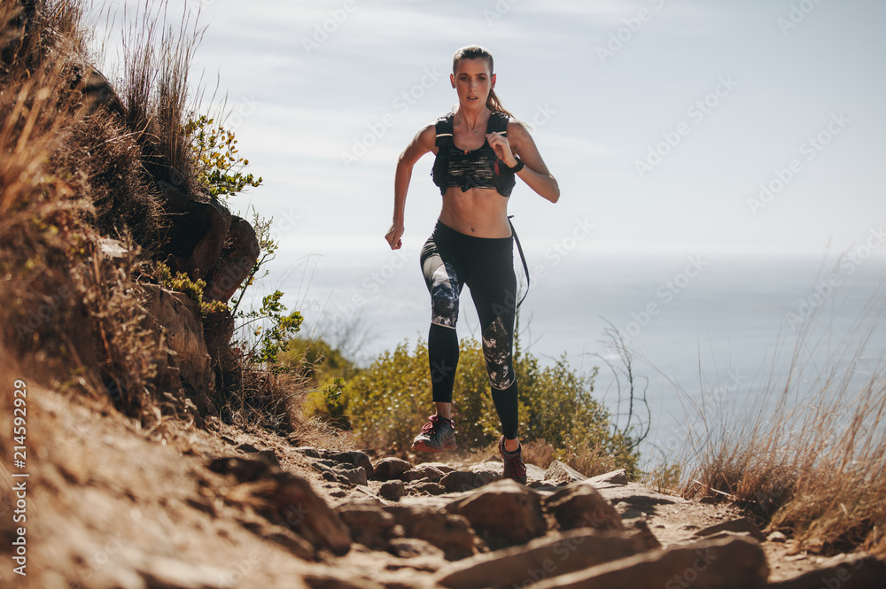 Woman running over rock trail on mountain - obrazy, fototapety, plakaty 