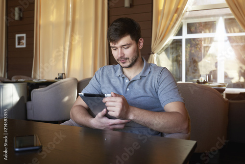 Creative male blogger monitoring personal website uploading account white pictures  sitting in coffee shop with modern touchpad connected to free wireless network photo