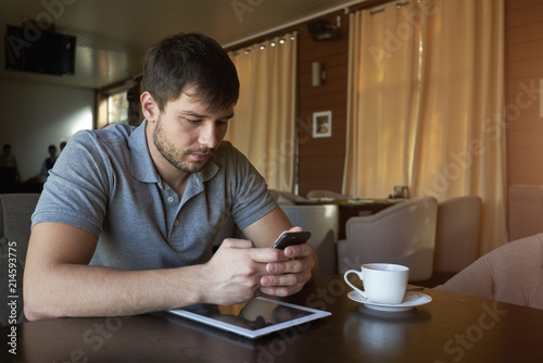 concentrated man searching information in internet while using modern smartphone pad and notebook. Concentrated smart student typing text on mobile phone to finding important news on website photo