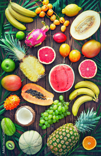Fototapeta Naklejka Na Ścianę i Meble -  Assortment of tropical fruits with leaves of palm trees and exotic plants on dark wooden background