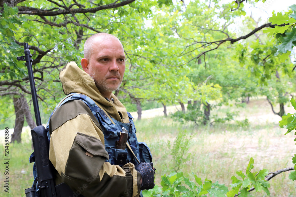 On the hunt. A man of 35-40 years old, a military hunter with a serious face is standing with a firearm in the forest.