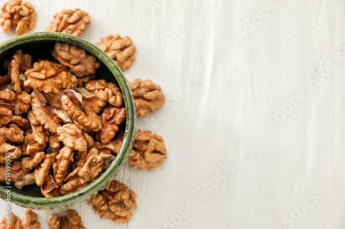 Bowl with fresh tasty walnuts on white wooden background