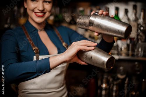 Smiling bartender girl holding two steel cocktail shakers