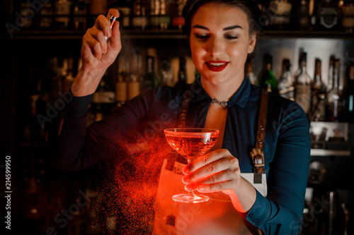 Beautiful bartender girl spraying on the delicious cocktail in her hand