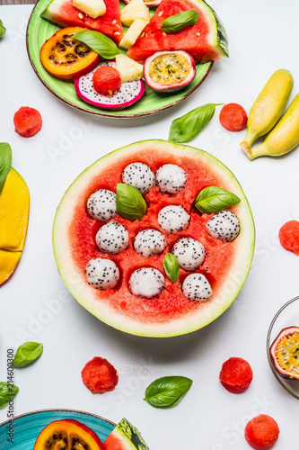 Fruits salad in watermelon bowl with ingredients on white background, top view. Healthy summer food and eating