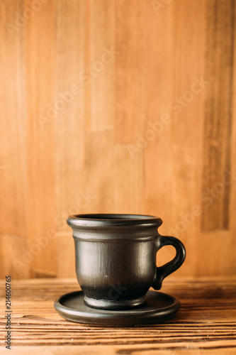 Black clay mug with coffee on a white background. a clay cup of black color on a wooden table. side view