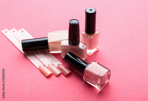 Bottles of varnish and artificial nails on color background