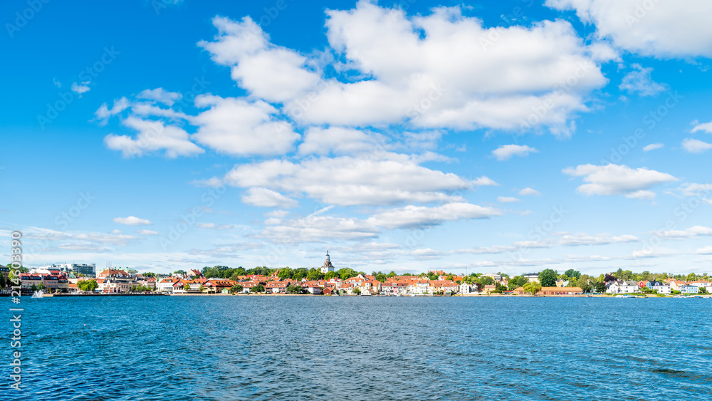 The coastal town of Vastervik, Sweden, on a sunny and fine summer morning. White clouds in the sky and a calm Baltic sea in the foreground. Logos removed.