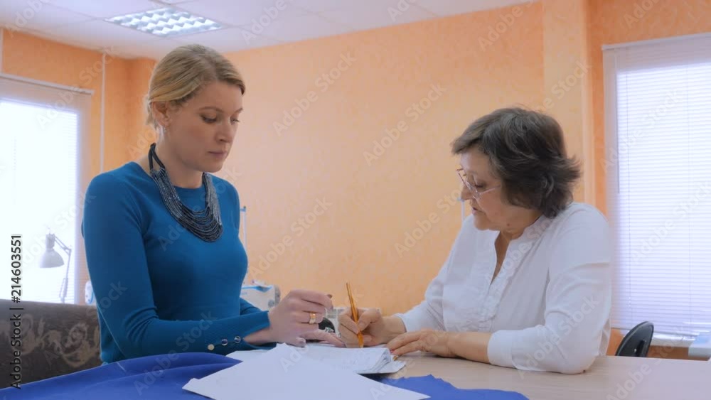 Two professional women tailors, designers discussing new couture collection at atelier, studio. Dressmaking, creativity and tailoring concept