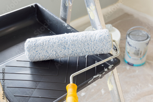 Fototapeta Naklejka Na Ścianę i Meble -  Painting and decorating with a roller and tray on a set of metal step ladders with cans of paint and a dust sheet in the background