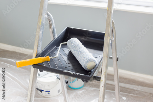 Fototapeta Naklejka Na Ścianę i Meble -  Painting and decorating with a roller and tray on a set of metal step ladders with cans of paint and a dust sheet in the background