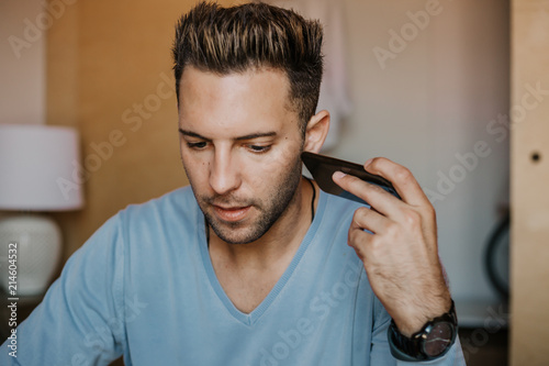 Handsome man using mobile smartphone for surfing web internet and sending audio message. Man using gadget at modern apartment