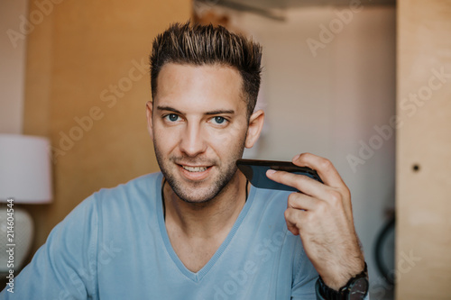 Handsome man using mobile smartphone for surfing web internet and sending audio message. Man using gadget at modern apartment photo