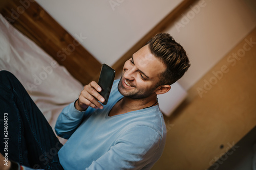 Handsome man using mobile smartphone for surfing web internet and sending audio message. Man using gadget at modern apartment photo