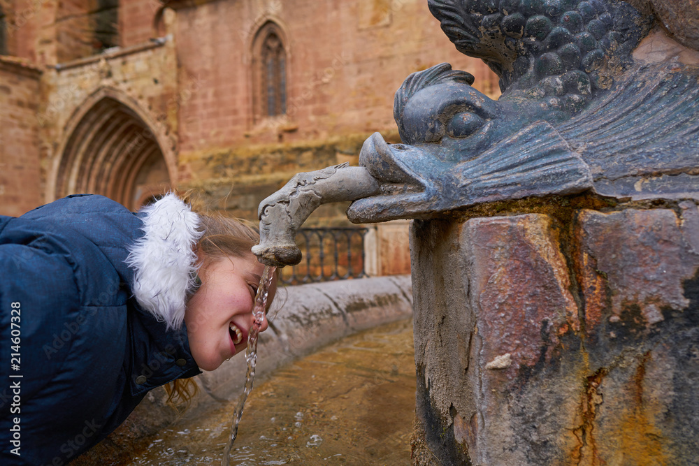 Blond kid girls drinking in old medieval fountain