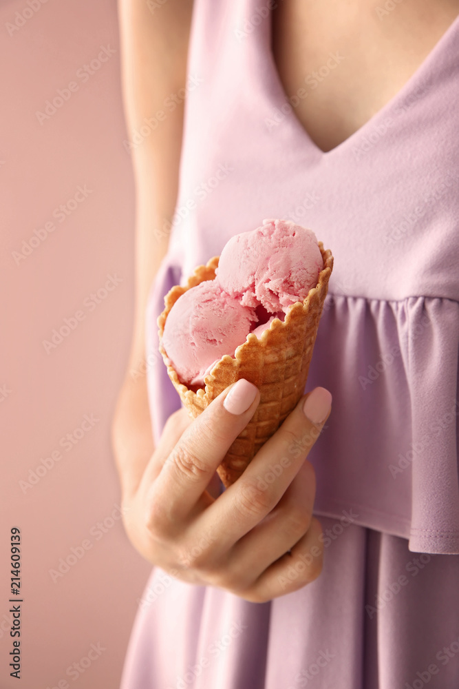Woman holding waffle cone with delicious strawberry ice-cream on color background, closeup Woman holding waffle cone with delicious strawberry ice-cream on color background, closeup