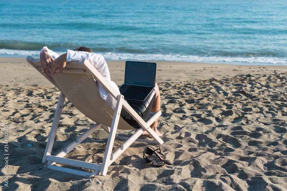 Young woman in office clothes with a laptop on the beach on a background of the sea in a summer sunny day. Concept Young woman in office clothes with a laptop on the beach on a background of the sea in a summer sunny day. Concept