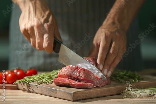 Man cutting raw meat on board in kitchen