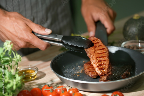 Man holding delicious roasted meat with tongs in kitchen, closeup photo