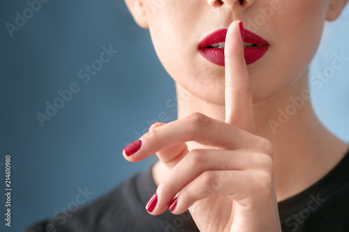Young woman with beautiful manicure showing silence gesture on color background  closeup