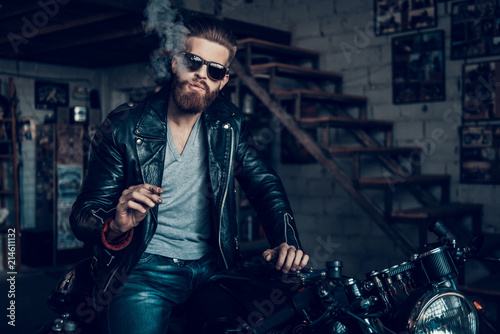 Foto Young Bearded Biker in Sunglasses Smoke Cigar.