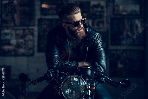 Young Biker in Sunglasses on Motorcycle in Garage. © VadimGuzhva