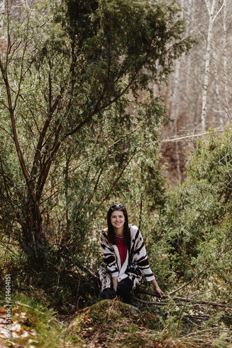 happy stylish hipster woman traveler, sitting in woods in mountains and smiling