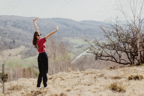 happy stylish hipster woman standing on top of hill mountain and raising hands up, cheerful moment of happiness