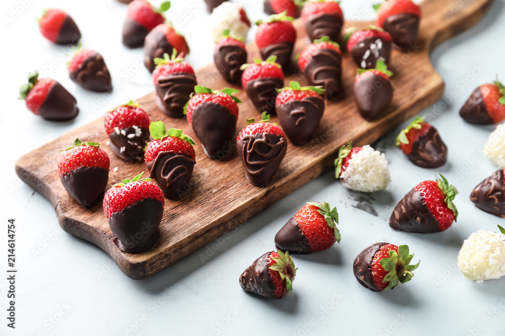 Wooden board with delicious strawberries covered with chocolate on color background