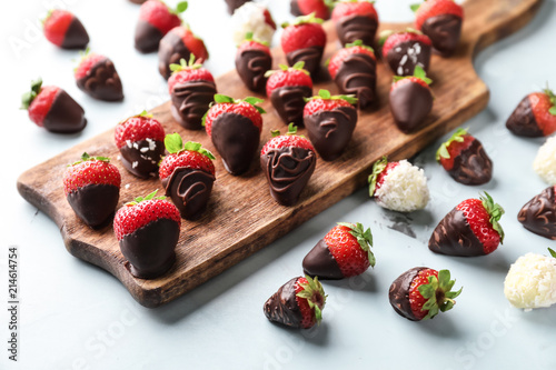 Wooden board with delicious strawberries covered with chocolate on color background